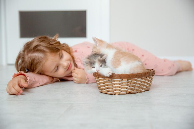 Uma garotinha em casa brincando com um gatinho no chão em uma cesta