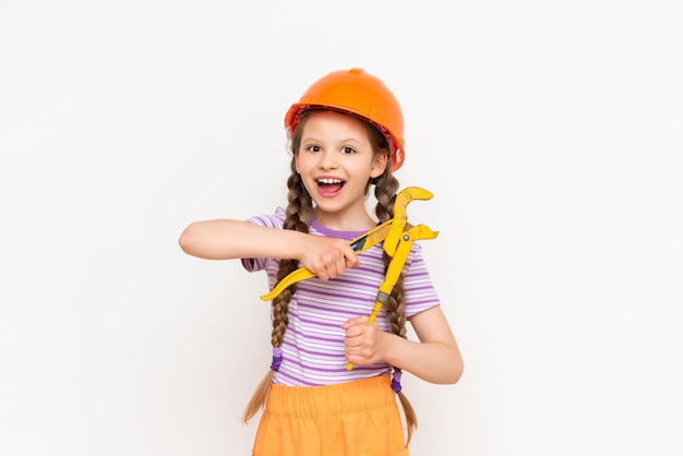 Uma garotinha em um capacete de construção laranja segura uma chave em um fundo branco isolado o conceito de renovação no quarto das crianças