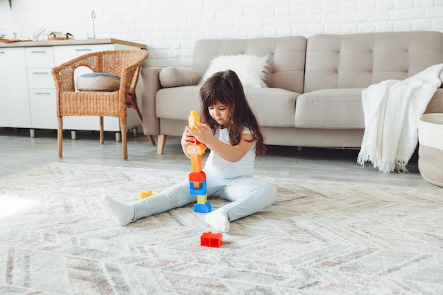 Uma garotinha está brincando com um construtor de cores em casa no chão