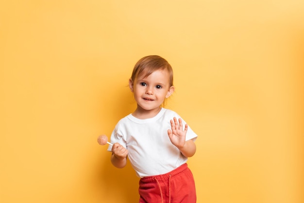 Uma garotinha está comendo um pirulito doce em uma vara Fundo amarelo O conceito de prevenção de cárie e diabetes em crianças