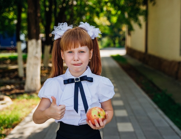 Uma garotinha está de pé no parque ou no pátio da escola segurando uma maçã nas mãos