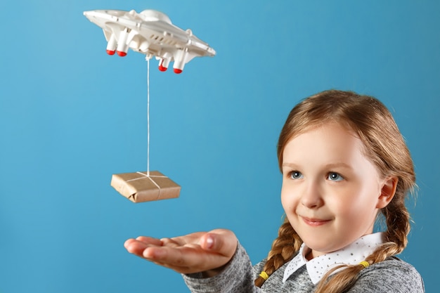 Uma garotinha estende a mão para uma caixa lotada amarrada a um quadricóptero.