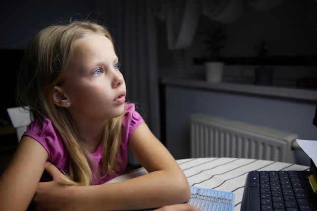 Uma garotinha europeia sorridente olha para a tela do monitor e sorri