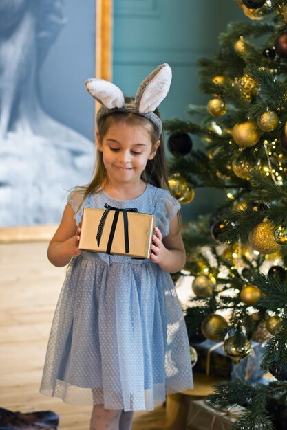 Foto uma garotinha fantasiada de coelho perto de uma árvore de natal com presentes