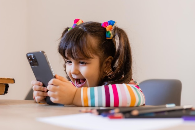Uma garotinha fofa está envolvida com um professor online por telefone Educação online de crianças Pré-escolares e gadgets