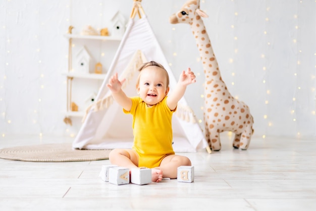 Uma garotinha fofa está sentada em uma sala de jogos infantil aconchegante e brilhante Têxteis para crianças