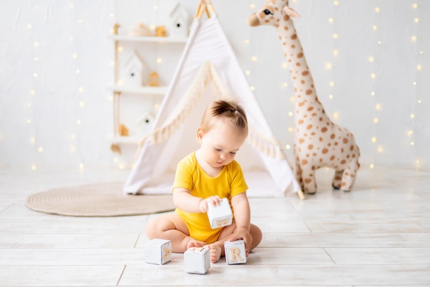 Uma garotinha fofa está sentada em uma sala de jogos infantil aconchegante e brilhante Têxteis para crianças