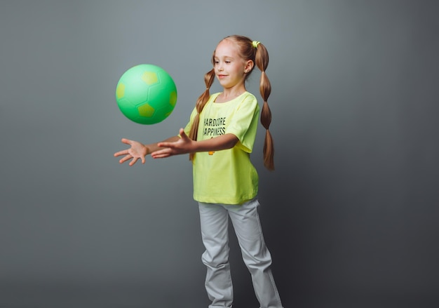 Uma garotinha joga uma bola isolada em um fundo cinza um pequeno atletaesportes infantis