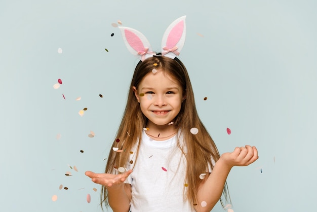 Uma garotinha linda em orelhas de coelho vomita confete conceito de férias de Páscoa