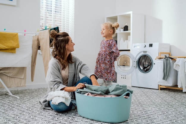 Uma garotinha loira de vestido passa tempo com a mãe na lavanderia