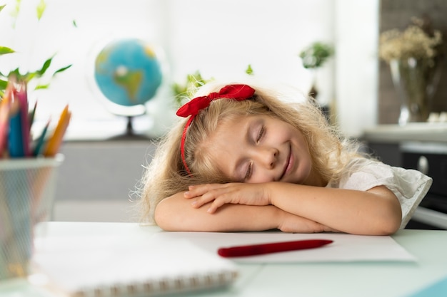 Uma garotinha loira está estudando cansada de estudar a criança deitada na mesa que a colegial está