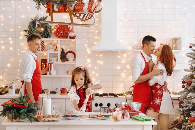 Uma garotinha na cozinha do ano novo faz massa e a família a ajuda