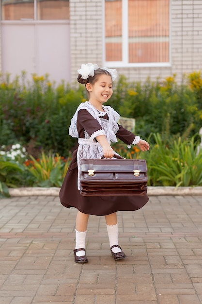 Uma garotinha na rua com o uniforme vintage com uma pasta fica perto da escola