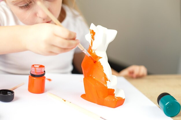 Uma garotinha pinta uma raposa de brinquedo feita de argila conceito DIY