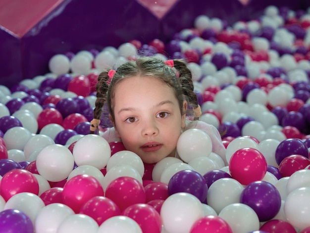 Foto uma garotinha se inclina para fora de bolas de plástico coloridas em uma grande piscina seca.