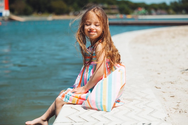 Uma garotinha se senta em um píer perto do lago da cidade ao ar livre nas férias de verão
