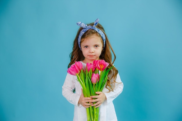 Uma garotinha segura um buquê de tulipas cor de rosa em um fundo azul