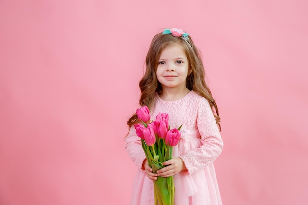 Uma garotinha segura um buquê de tulipas cor de rosa em um fundo rosa