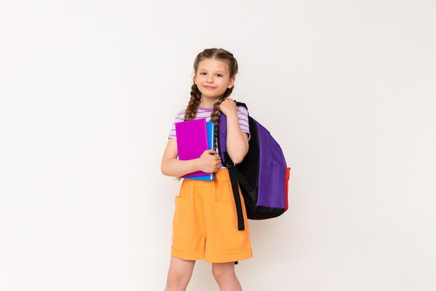 Uma garotinha segura uma bolsa nas costas e livros nas mãos e sorri aulas de férias de verão
