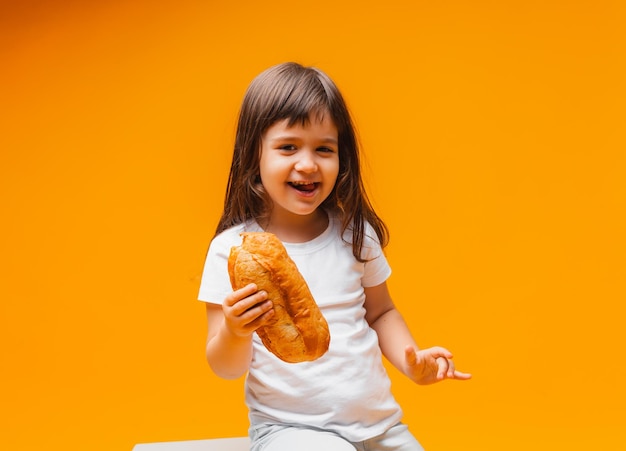 Uma garotinha senta-se em um cubo sobre um fundo amarelo e come um pão de produtos naturais de alimentos saudáveis