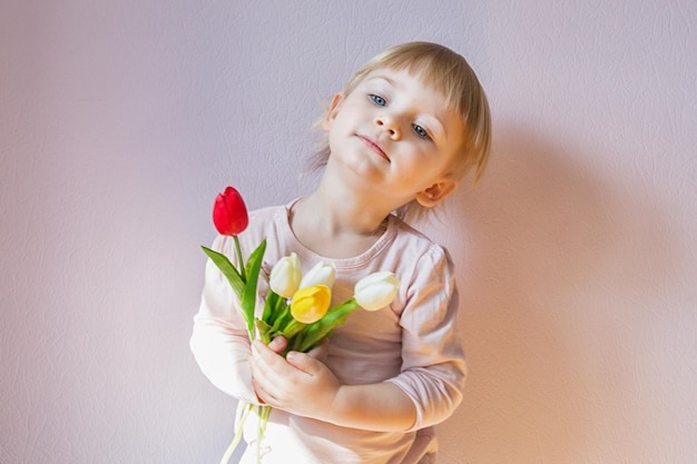 Uma garotinha séria com cabelo loiro está segurando um buquê de tulipas nas mãos