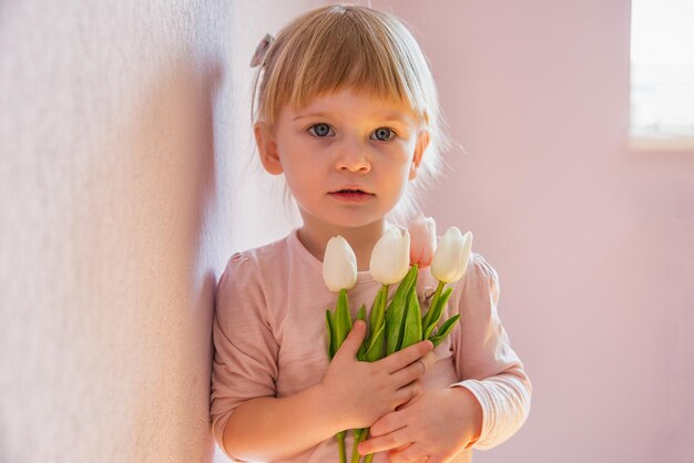 Uma garotinha séria está segurando um buquê de tulipas nas mãos