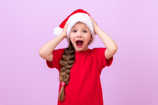 Uma garotinha surpresa agarrou seu chapéu de natal em um fundo roxo isolado.