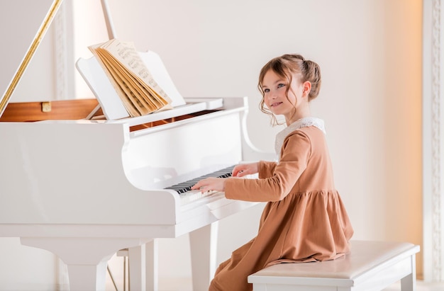 Uma garotinha toca um grande piano branco em uma sala ensolarada
