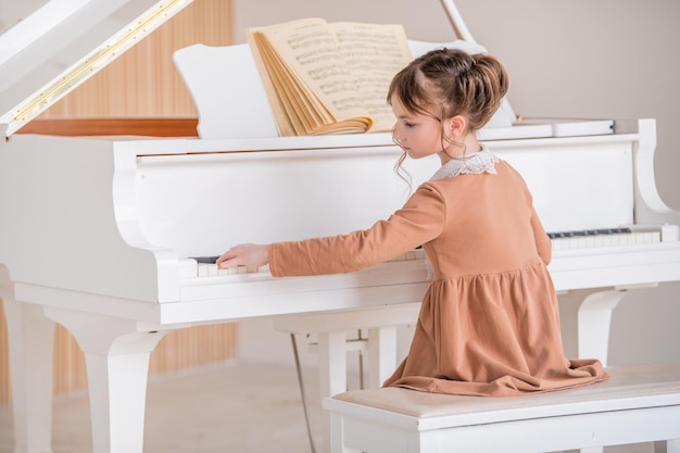 Uma garotinha toca um grande piano branco em uma sala ensolarada