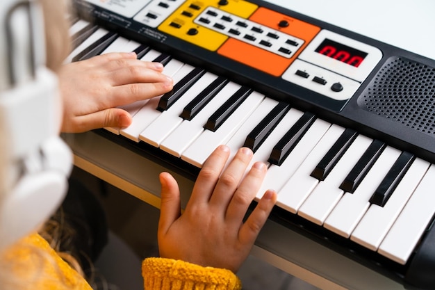 Uma garotinha tocando o sintetizador o conceito de ensinar as mãos de música para crianças closeup