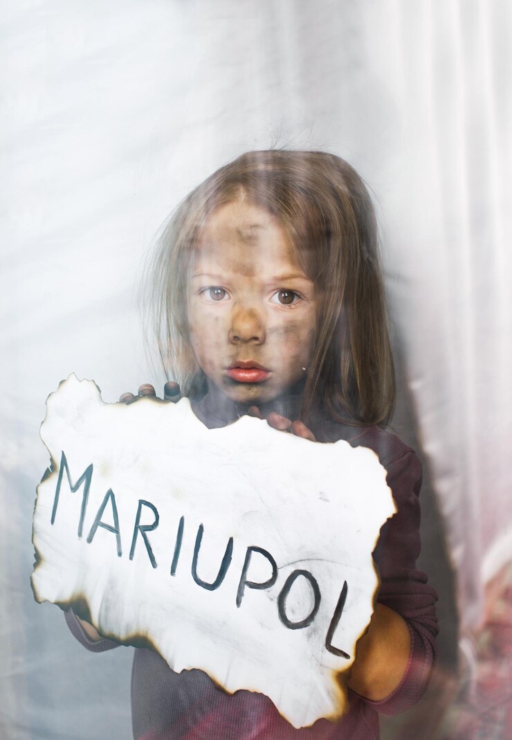 Foto uma garotinha ucraniana com olhos tristes está atrás do vidro segurando um pedaço de papel queimado com a inscrição mariupol children and war