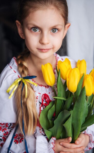 Uma garotinha ucraniana em roupas tradicionais tem tulipas amarelas nas mãos