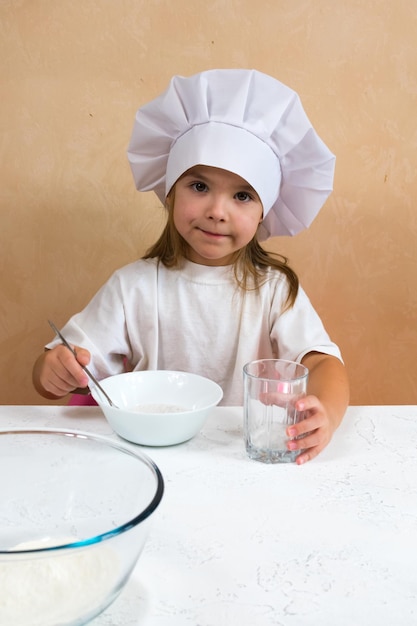 Uma garotinha vestida de cozinheira amassa a massa Conceito de desenvolvimento infantil O desenvolvimento de habilidades motoras finas das mãos A criança adora se diverte estudando e brincando na cozinha