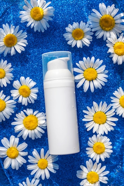 Uma garrafa branca com produtos cosméticos e flores de camomila em fundo azul brilhante Conceito cosmético de beleza orgânica natural Vista frontal