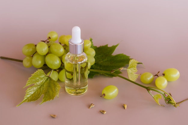 Uma garrafa com um conta-gotas com um produto orgânico à base de sementes de uva contra uvas amarelas maduras bio cosméticos naturais fundo bege