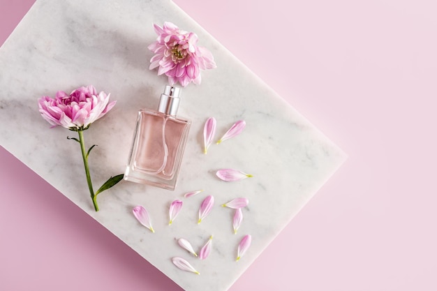 Uma garrafa com um produto cosmético ou perfume encontra-se em um pódio branco de mármore com pétalas e flores de um lilás uma apresentação do produto de espaço de cópia