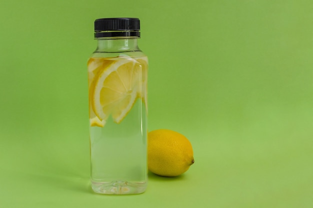 Uma garrafa de água com rodelas de limão sobre fundo verde com espaço de cópia