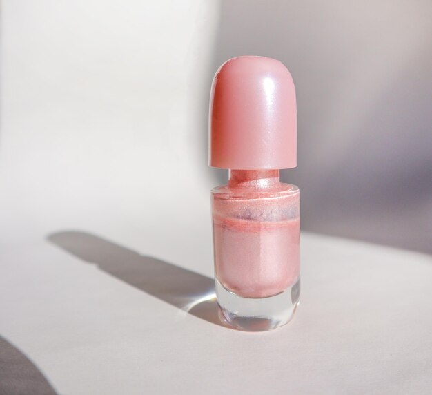 Uma garrafa de esmalte rosa em uma superfície branca com sombra o conceito de beleza na moda