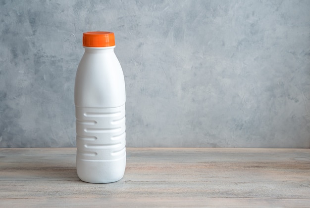 Uma garrafa de leite branca com uma tampa laranja em um fundo cinza.