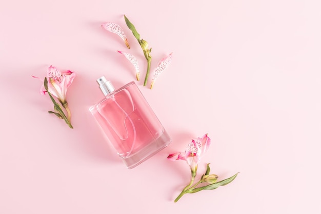 Uma garrafa de perfume feminino ou água de toalete em um fundo rosa entre os botões da apresentação do produto astromeria uma cópia da vista superior do espaço