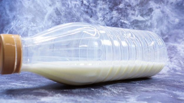 Uma garrafa de plástico semivazia de leite fresco regular está em um mármore cinza escuro ou fundo de concreto. Vista frontal do close-up. Conceito do dia mundial do leite. Fluido nutritivo.