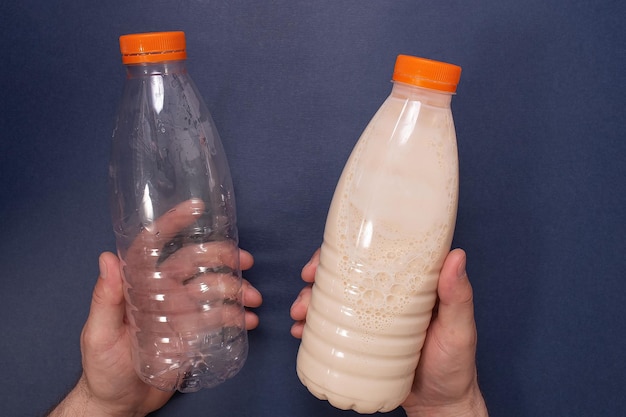 Uma garrafa de plástico vazia e uma garrafa de leite nas mãos do homem em um fundo azul Alimentos e bebidas
