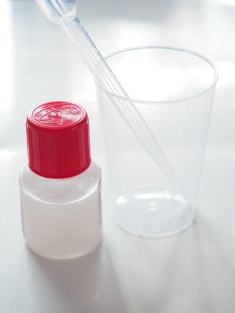 Uma garrafa de plástico vermelha com tampa vermelha fica ao lado de um copo de plástico transparente.