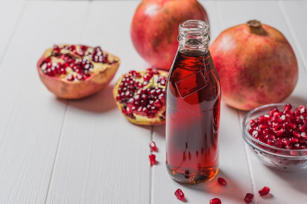 Uma garrafa de suco de romã e romãs maduras em uma mesa branca. Bebida útil para a saúde.