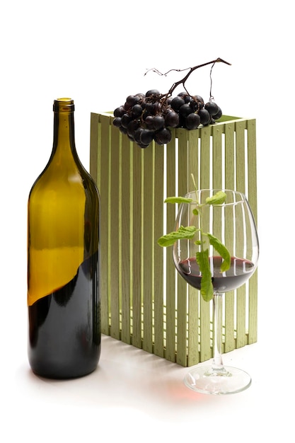 Uma garrafa de vinho e cachos de uvas maduras em um copo sobre fundo branco