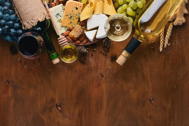 Uma garrafa de vinho e uma grande variedade de queijos mel nozes e especiarias em uma mesa de madeira Vista superior Espaço livre para texto