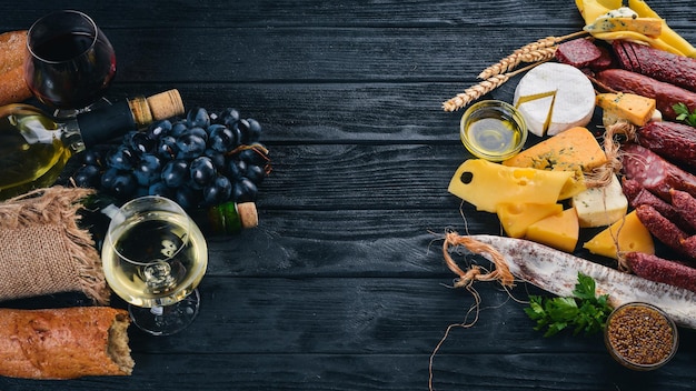 Uma garrafa de vinho, queijos e enchidos tradicionais em um fundo de madeira. Queijo brie, queijo azul, gorgonzola, fuete, salame. Espaço livre para texto. Vista do topo.