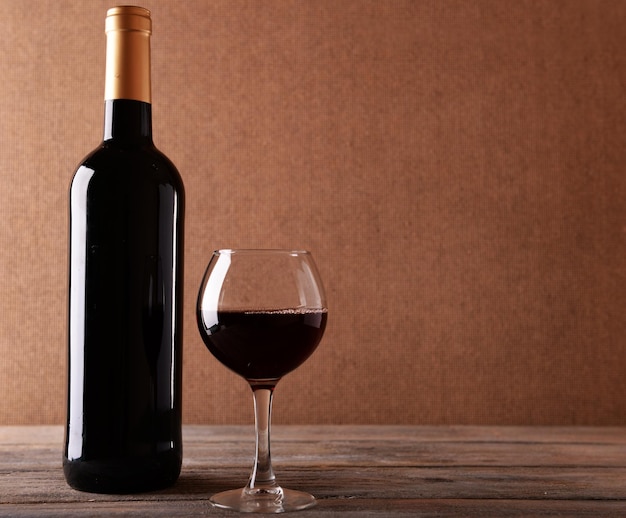 Uma garrafa de vinho tinto e um copo em uma mesa de madeira