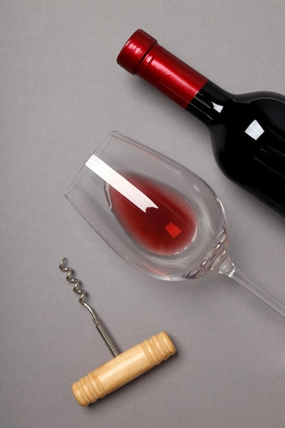 Uma garrafa de vinho, um copo e um saca-rolhas sobre um fundo cinzento.