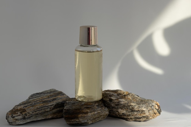Uma garrafa de xampu de gel de banho de óleo essencial na rocha contra folha de monstera ou sombras diagonais do sol
